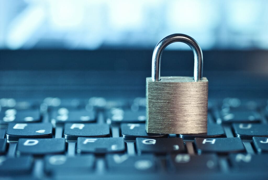 A metal padlock sits on a computer keyboard, symbolizing cybersecurity and data protection in payment technology. The image is focused on the lock with blurred keys in the background.