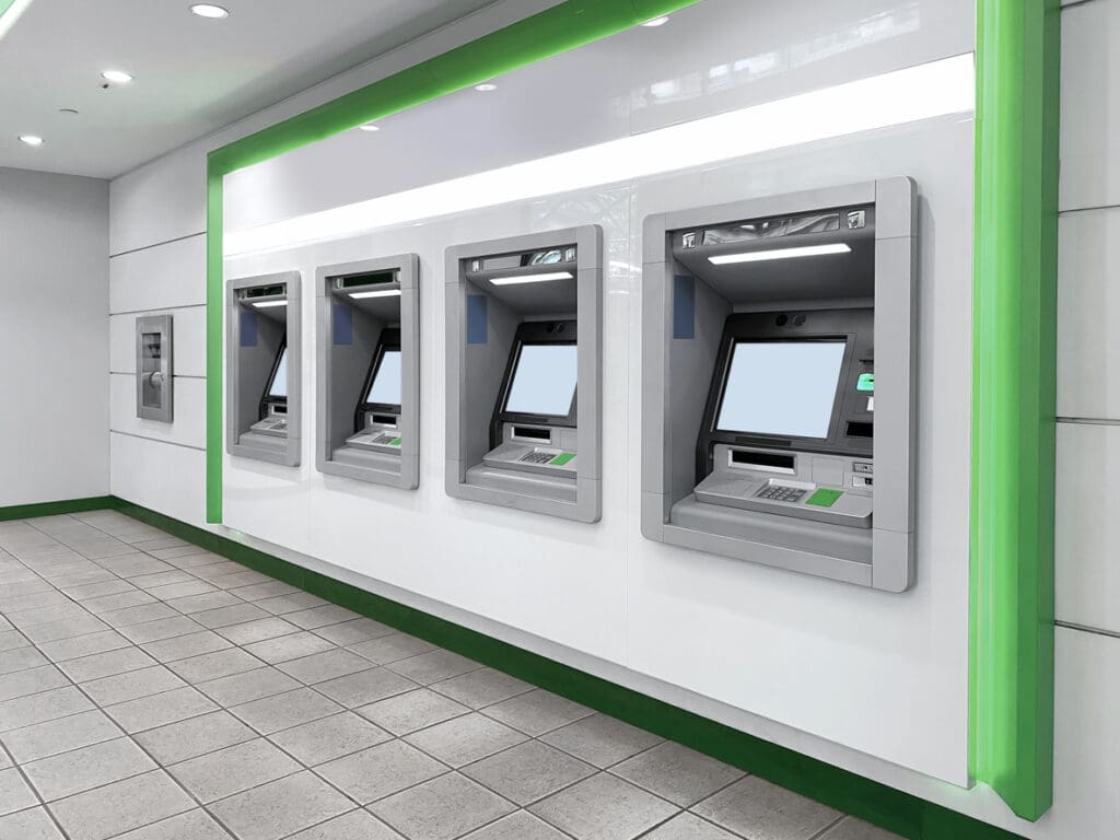 A row of modern cash machines built into a white wall with green accents, located in a clean, well-lit indoor banking area with tiled floors—perfect for business owners seeking convenient ways to maximize profits. No people are present.