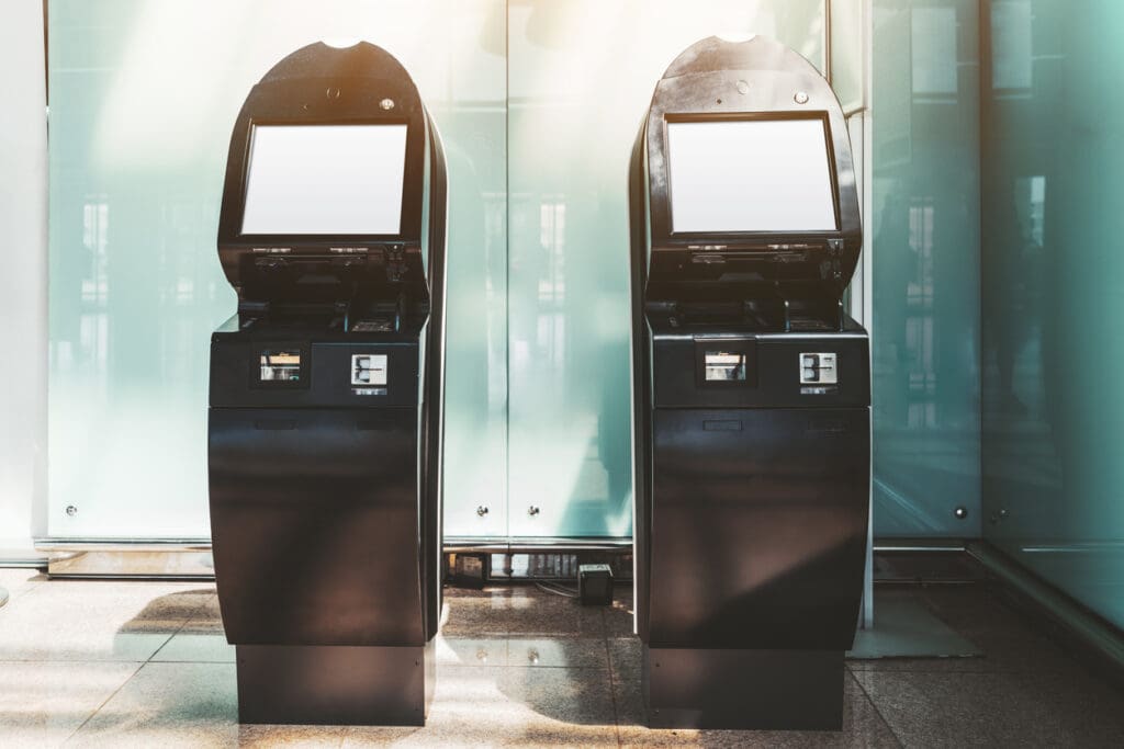 Two black Reverse ATMs with blank screens stand side by side indoors on a shiny floor, sunlight streaming through large glass panels in the background—ideal for cash to card payment technology.