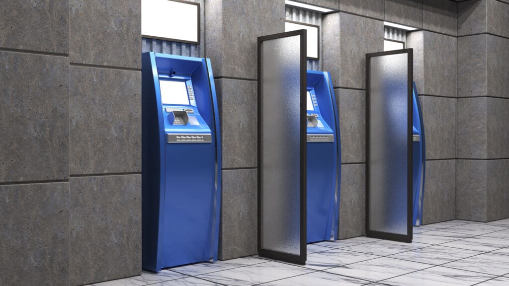 Three blue cash machines are lined up against a gray tiled wall, separated by frosted glass privacy screens. The floor is white with dark veins, and overhead lights illuminate the machines for business owners looking to maximize profits.
