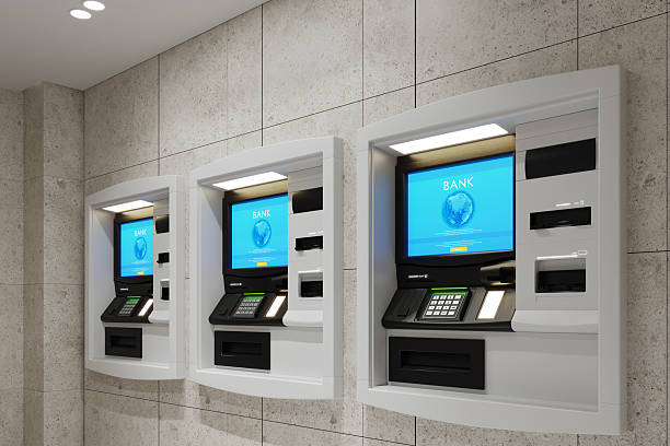 Three modern ATMs are mounted side by side on a tiled wall, each displaying a blue screen with the word BANK and a globe image—a prime spot for anyone considering ATM investment. The area is brightly lit.