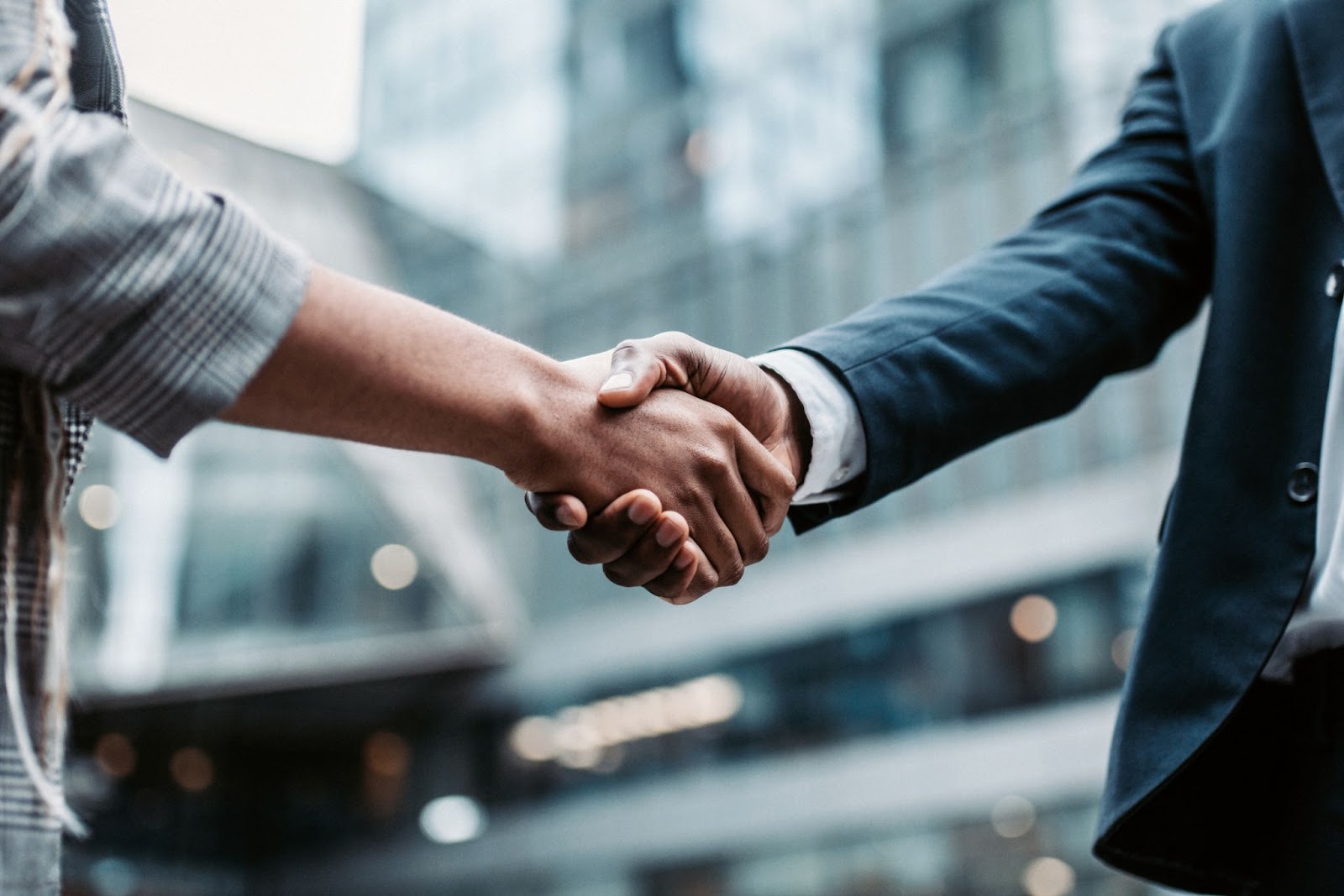 Two people in business attire shaking hands outdoors in front of a modern glass building, symbolizing agreement or partnership between the best ATM service providers.