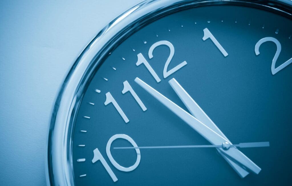 Close-up of a wall clock showing the time as 10:55, with a blue tint over the image—reminding viewers of an upcoming compliance deadline in New York.
